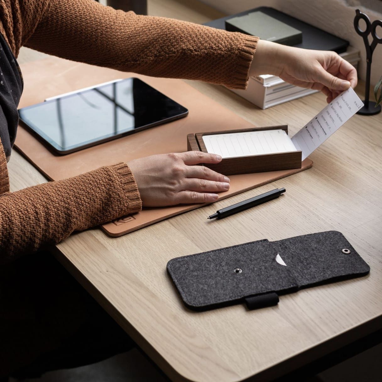 Person sitting at a wooden desk with paper note organizer, pencil and tablet.